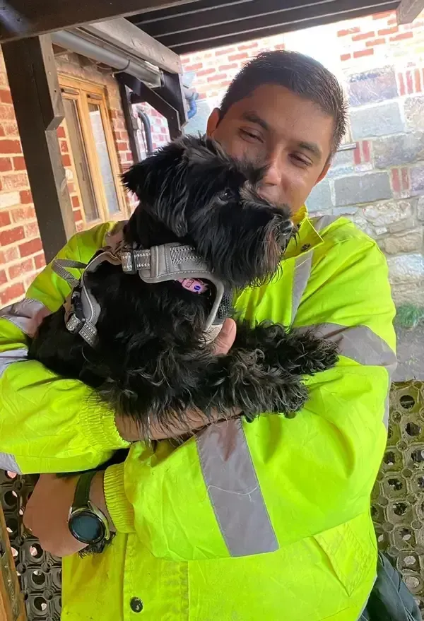 A staff member cuddling a small black dog at The Barn